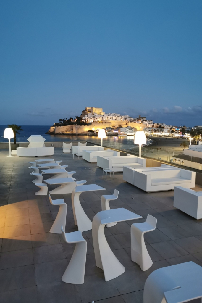 Terraza rooftop de Hoteles Mediterráneo de noche con sofás blancos y vistas al Castillo del Papa Luna iluminado en Peñíscola